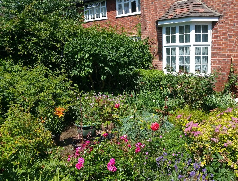 Cottage-style front garden border in full flower outside a red-brick house